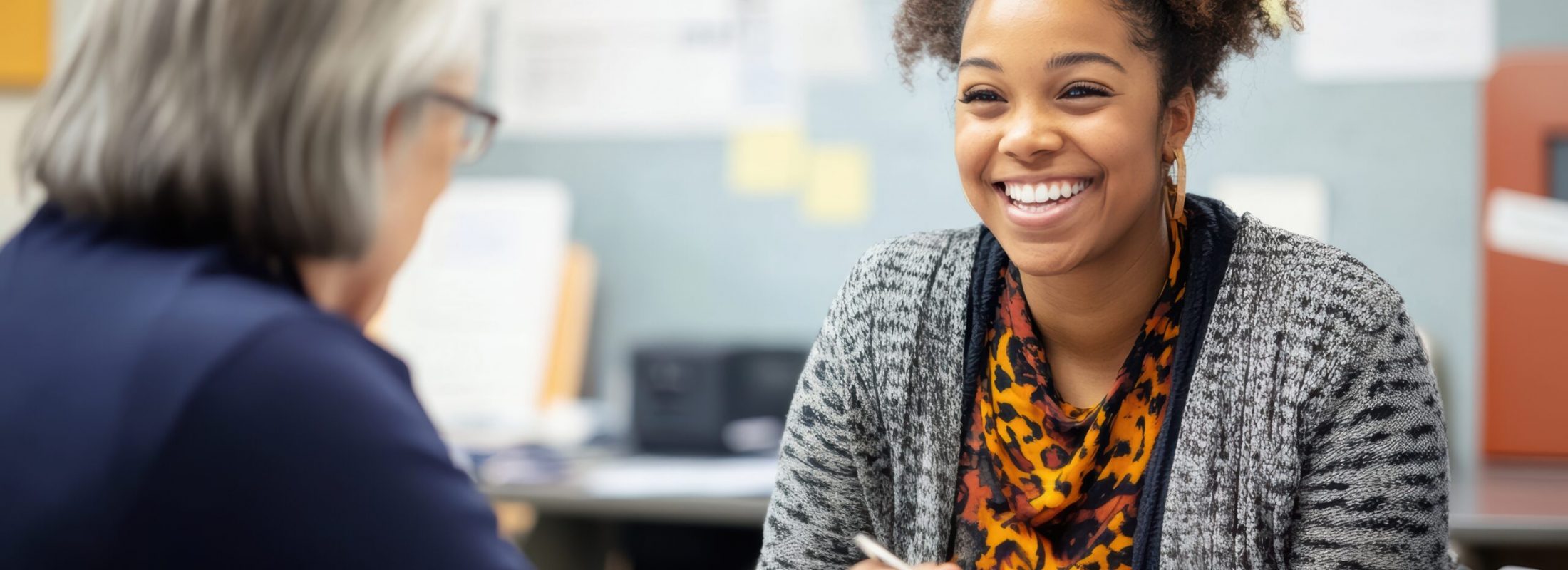 A social worker is smiling and actively listening to a client during a discussion in a community center. The environment is supportive and focused on assistance and guidance