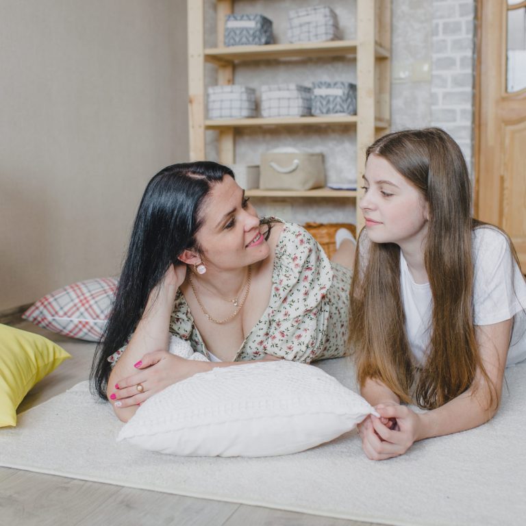 A smiling mother and her teenage daughter are lying on the floor and looking at each other. happy family